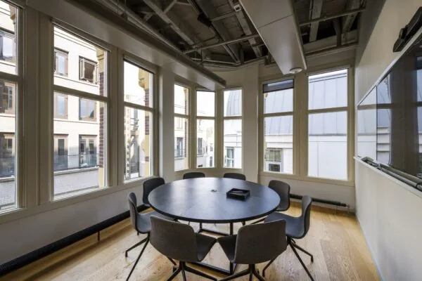 Vergaderruimte met ronde tafel en zes stoelen, omringd door grote ramen in een pand aan de Sint-Jorissteeg.